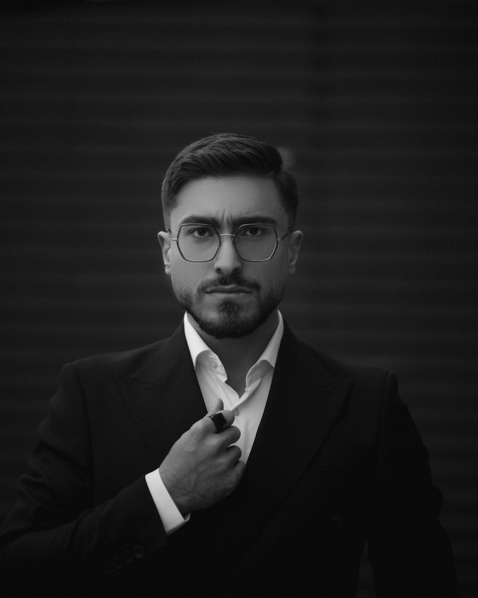 A man in a suit and glasses is straightening his tie